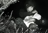 A mother sits among bushes in a field just north of the US-Mexico border